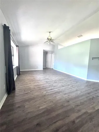 an empty room with wooden floor and a kitchen view