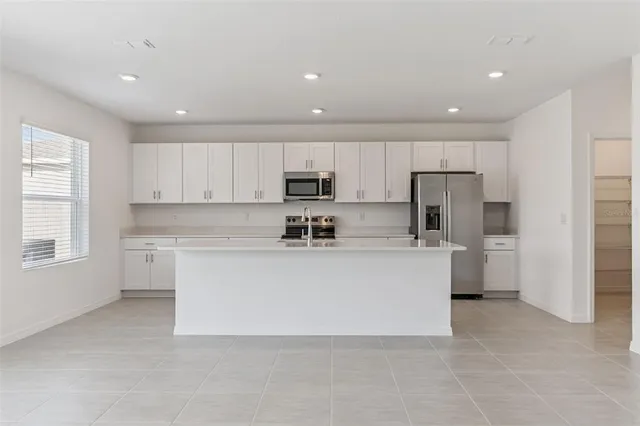 a large white kitchen with stainless steel appliances granite countertop a stove a sink a refrigerator and a cabinets