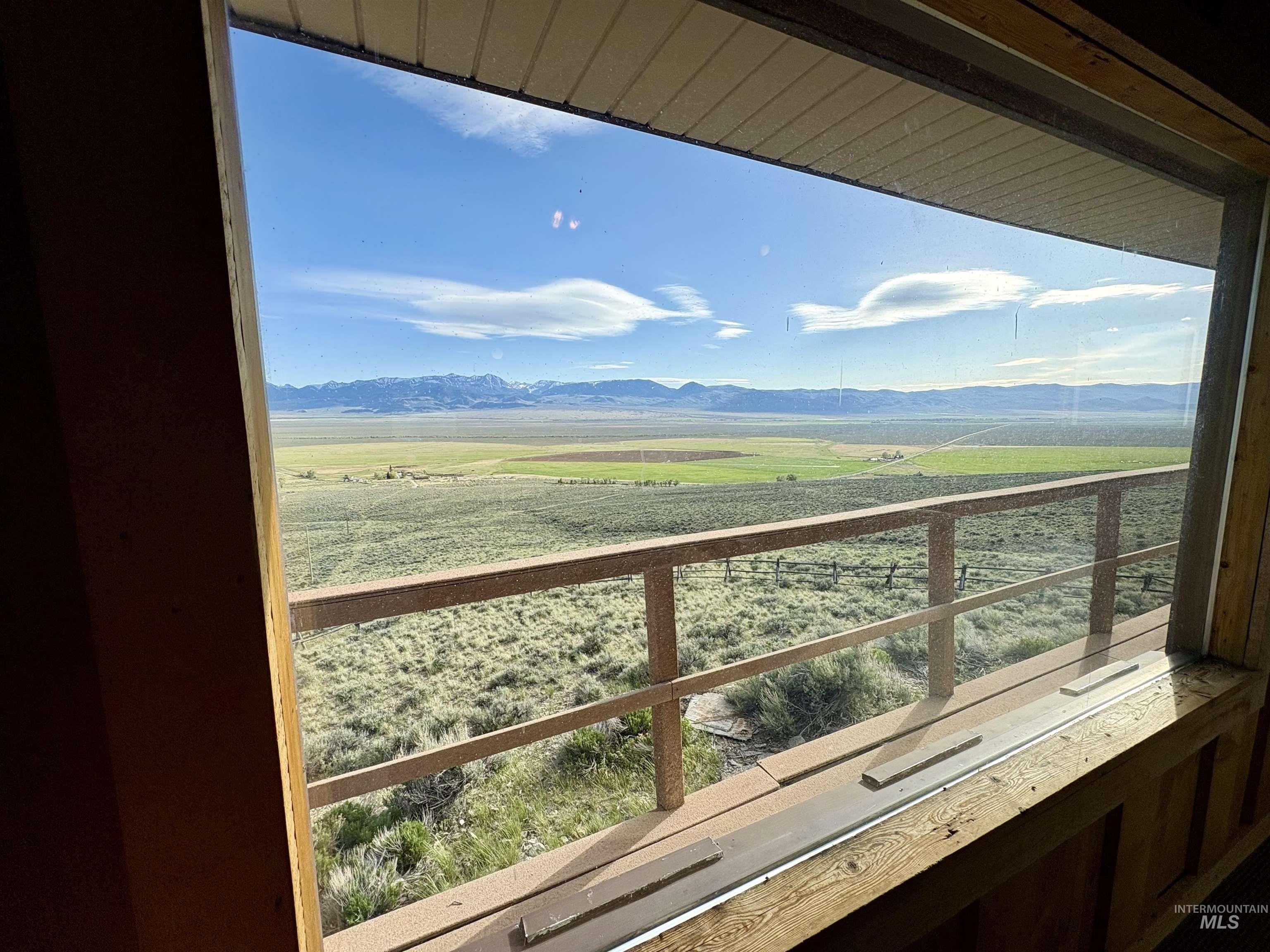 2040 Pahsimeroi River Road May, ID 83253 - Photo 13 of 29 Expansive landscape through a large picture window, featuring distant snow-capped mountains, verdant fields, and a railing on an outdoor space