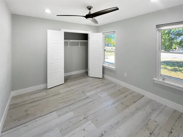 an empty room with wooden floor ceiling fan and windows