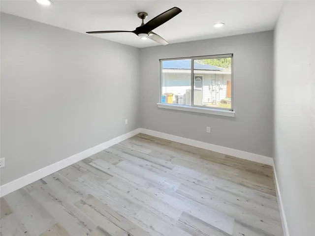 an empty room with wooden floor ceiling fan and windows