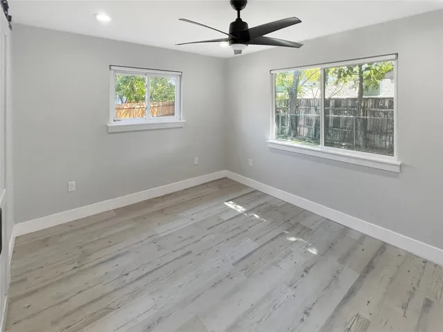an empty room with wooden floor fan and windows