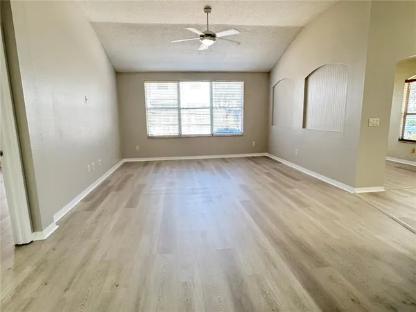 an empty room with wooden floor ceiling fan and windows