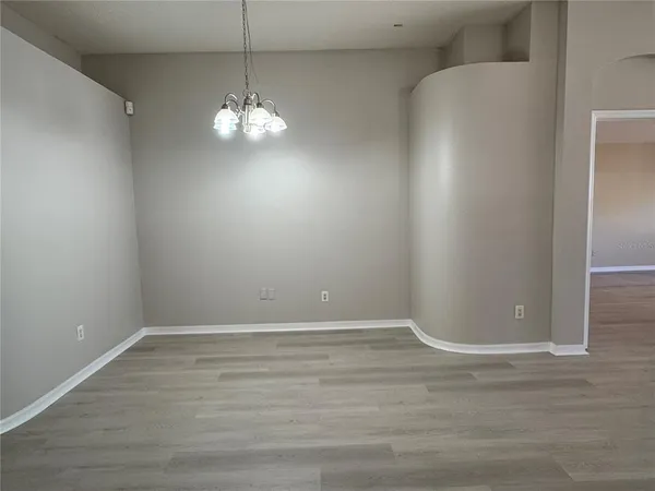 a view of an empty room with chandelier fan and kitchen view