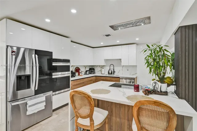 a kitchen with stainless steel appliances a sink a stove a refrigerator and chairs