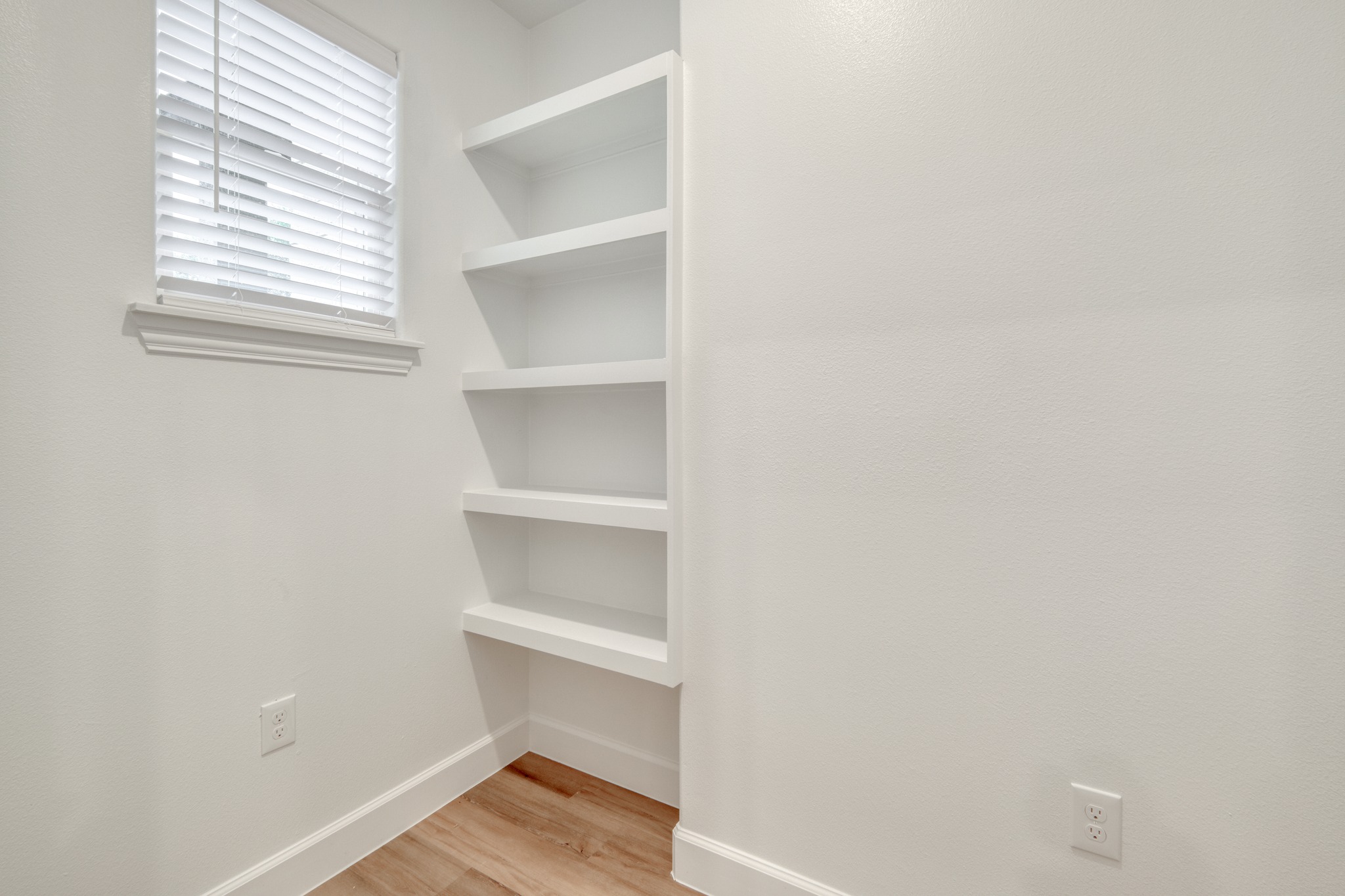 116 Pine Point Cove Elgin, TX 78621 - Photo 23 of 27 Built-in shelving unit with five white shelves, wood-finish flooring, and a window with blinds