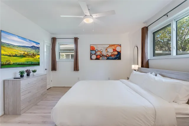a bedroom with a flat screen tv on dresser and a window