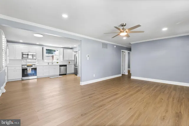 a view of an empty room and kitchen view with wooden floor