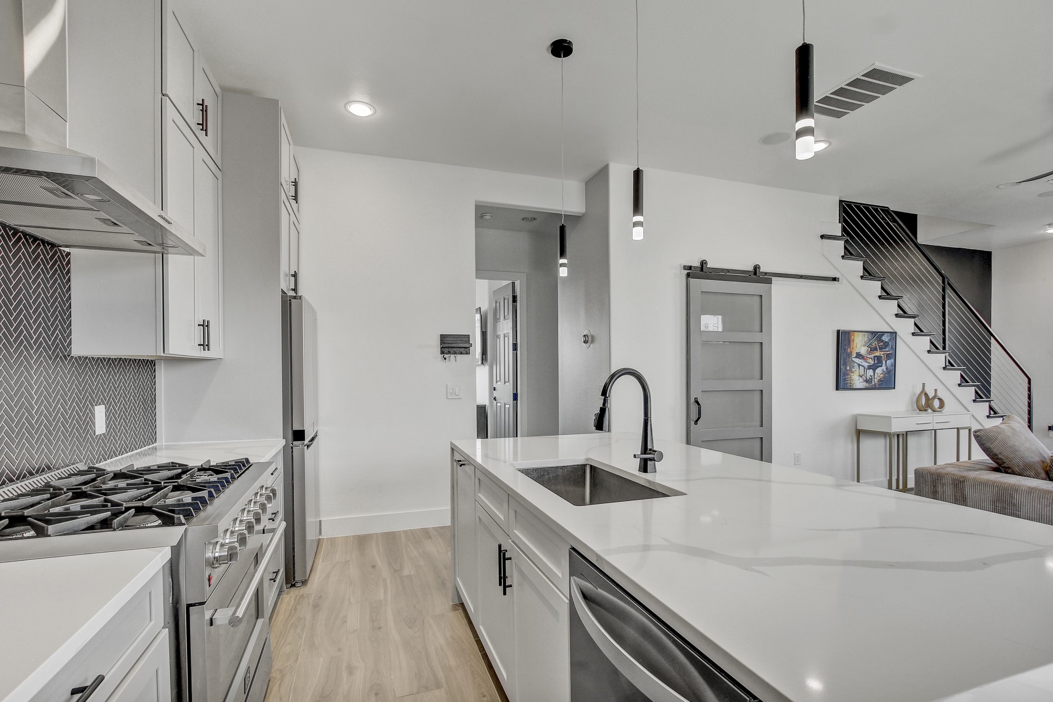 4703 Louis Avenue, Unit A Austin, TX 78721 - Photo 14 of 35 Kitchen with stainless steel appliances, a barn door, white cabinets, a kitchen island with sink, and decorative light fixtures