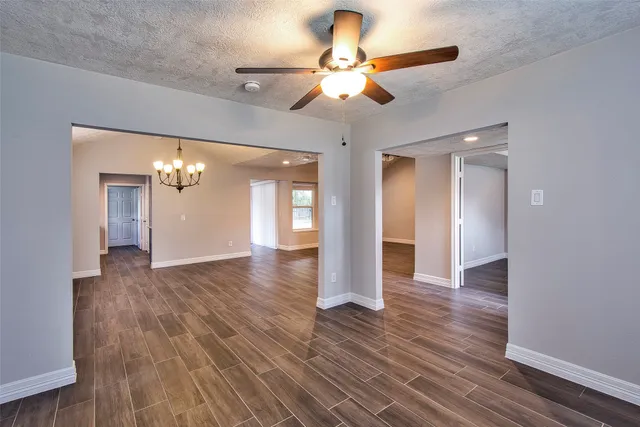 a view of an empty room with wooden floor and a ceiling fan
