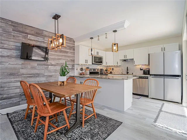 a kitchen with stainless steel appliances kitchen island granite countertop a dining table chairs and a refrigerator