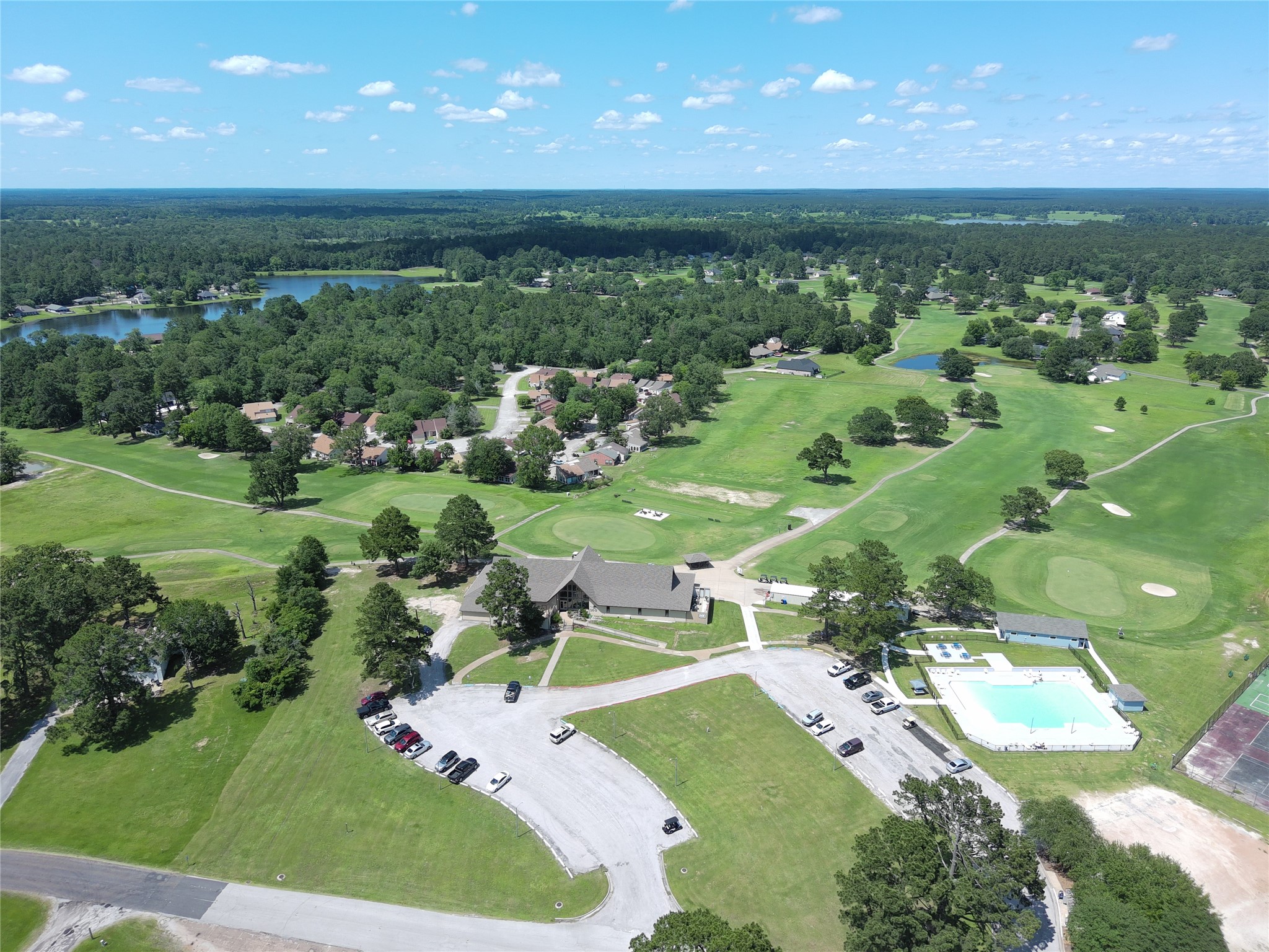59 Oakridge South Trinity, TX 75862 - Photo 8 of 10 This aerial photo showcases a serene residential area with lush greenery, a golf course, and a nearby lake. The community features a clubhouse, swimming pool, and ample outdoor space, offering a tranquil and recreational living environment.