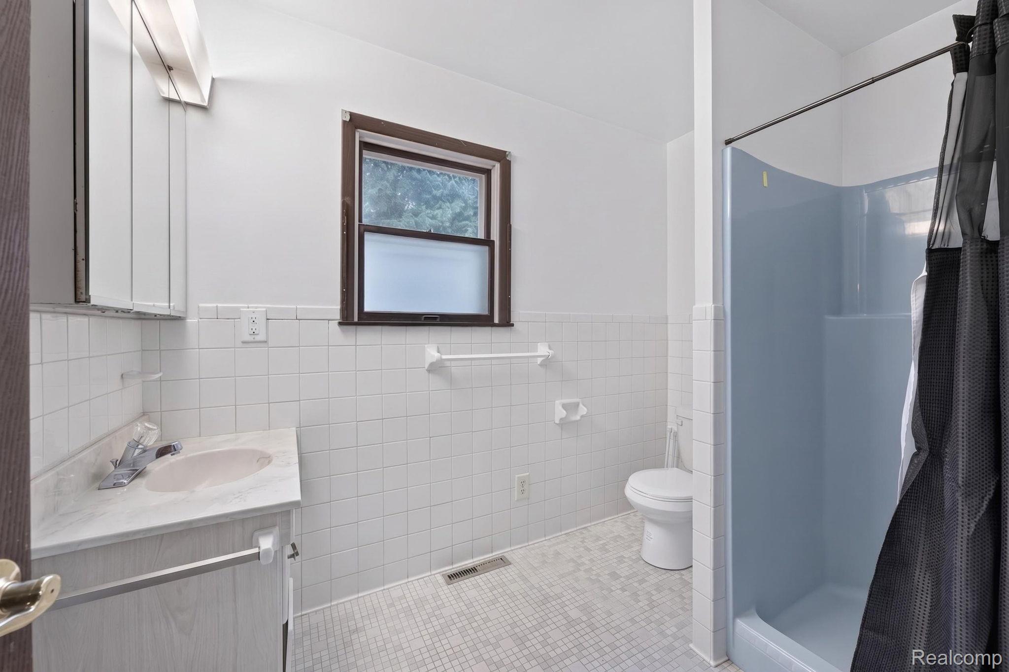 5330 Sheridan Road Saginaw, MI 48601 - Photo 38 of 50 Bathroom featuring a single vanity with a laminate countertop, a toilet, and a stand-up shower with a gray surround