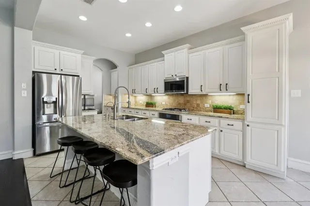 a kitchen with stainless steel appliances granite countertop a stove top oven a refrigerator a sink and white cabinets