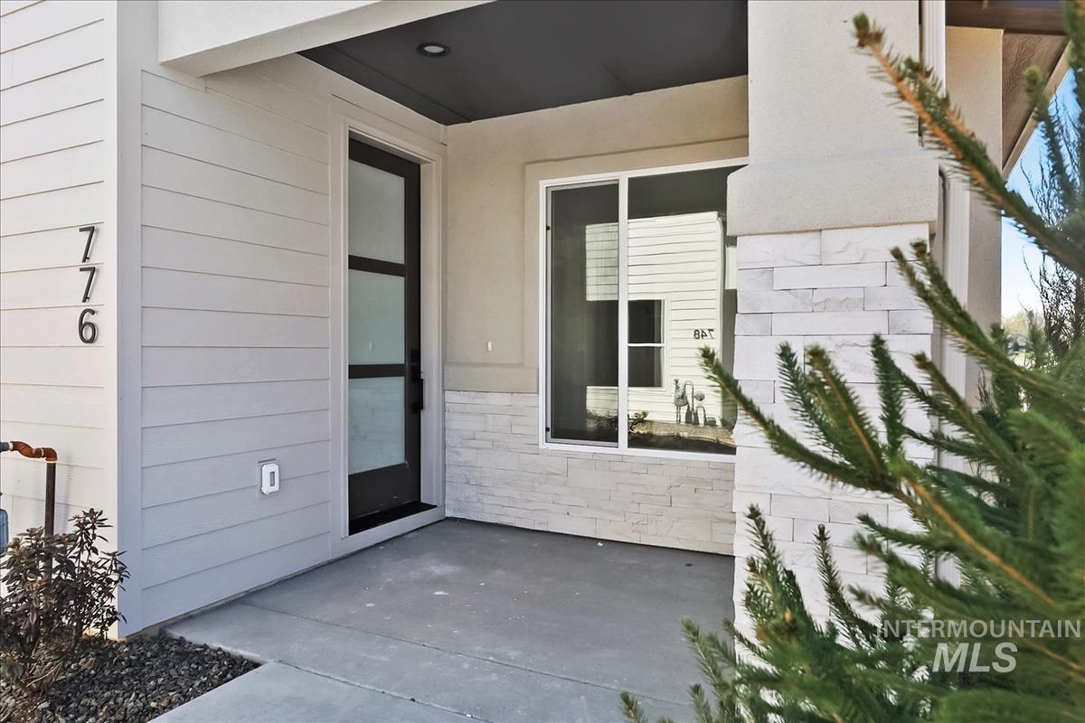 776 South Calhoun Lane Star, ID 83669 - Photo 3 of 49 Modern entry featuring light gray horizontal siding, stacked stone accents, a dark-framed glass paneled door, a large window, and a covered porch with a dark soffit
