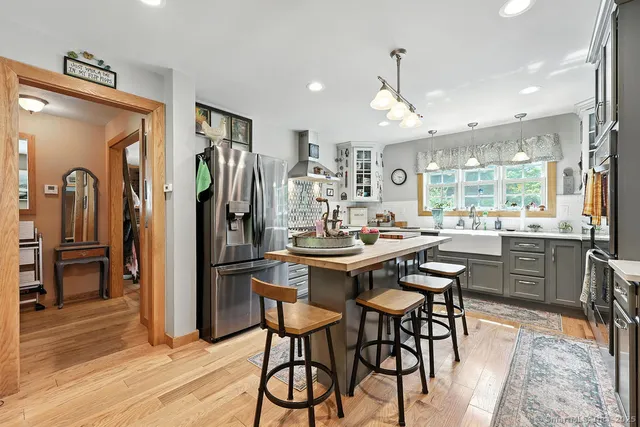 a kitchen with stainless steel appliances granite countertop a refrigerator a stove a sink a dining table and chairs with wooden floor