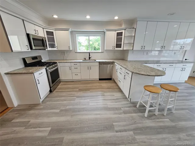 a large kitchen with stainless steel appliances granite countertop a stove a sink a microwave a window and white cabinets