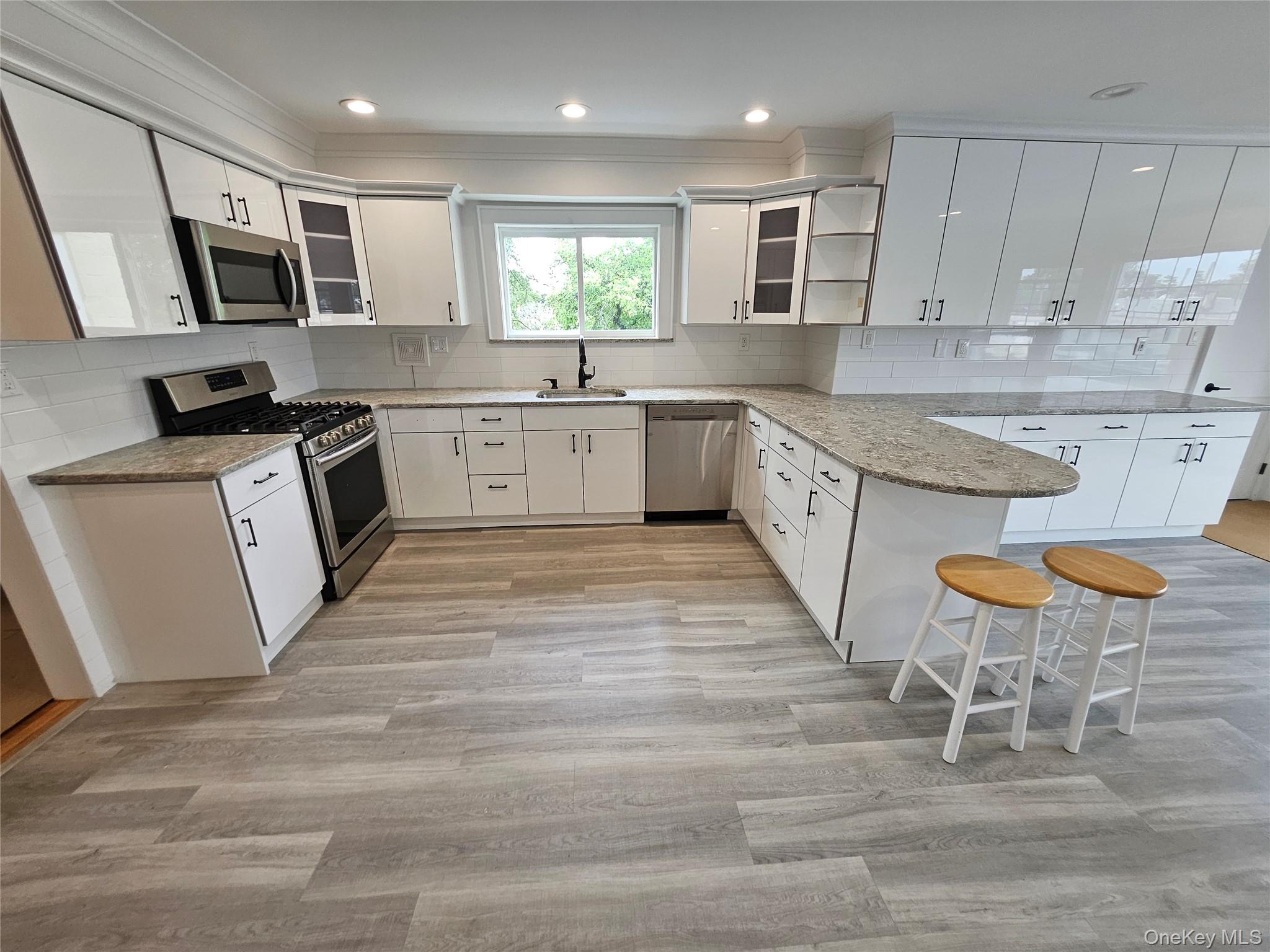 a large kitchen with stainless steel appliances granite countertop a stove a sink a microwave a window and white cabinets