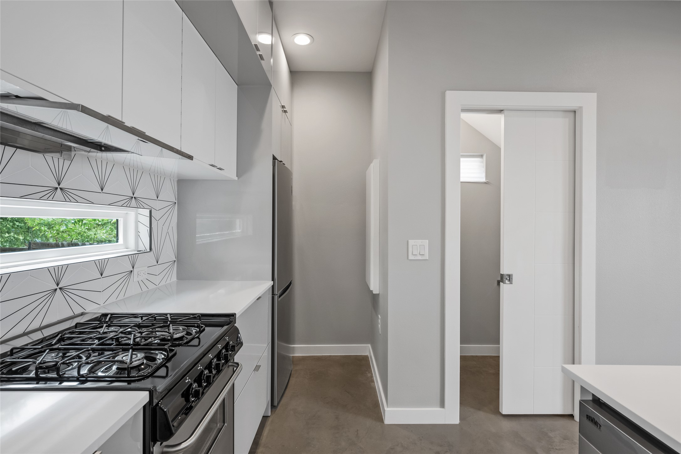 2108 Tillery Street, Unit 16 Austin, TX 78723 - Photo 5 of 15 Galley kitchen featuring glossy white cabinetry, integrated stainless-steel appliances, a gas range with a range hood, geometric tile backsplash, and a horizontal window