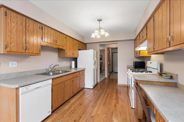 a kitchen with stainless steel appliances granite countertop a refrigerator a sink dishwasher a stove and white countertops with wooden floor