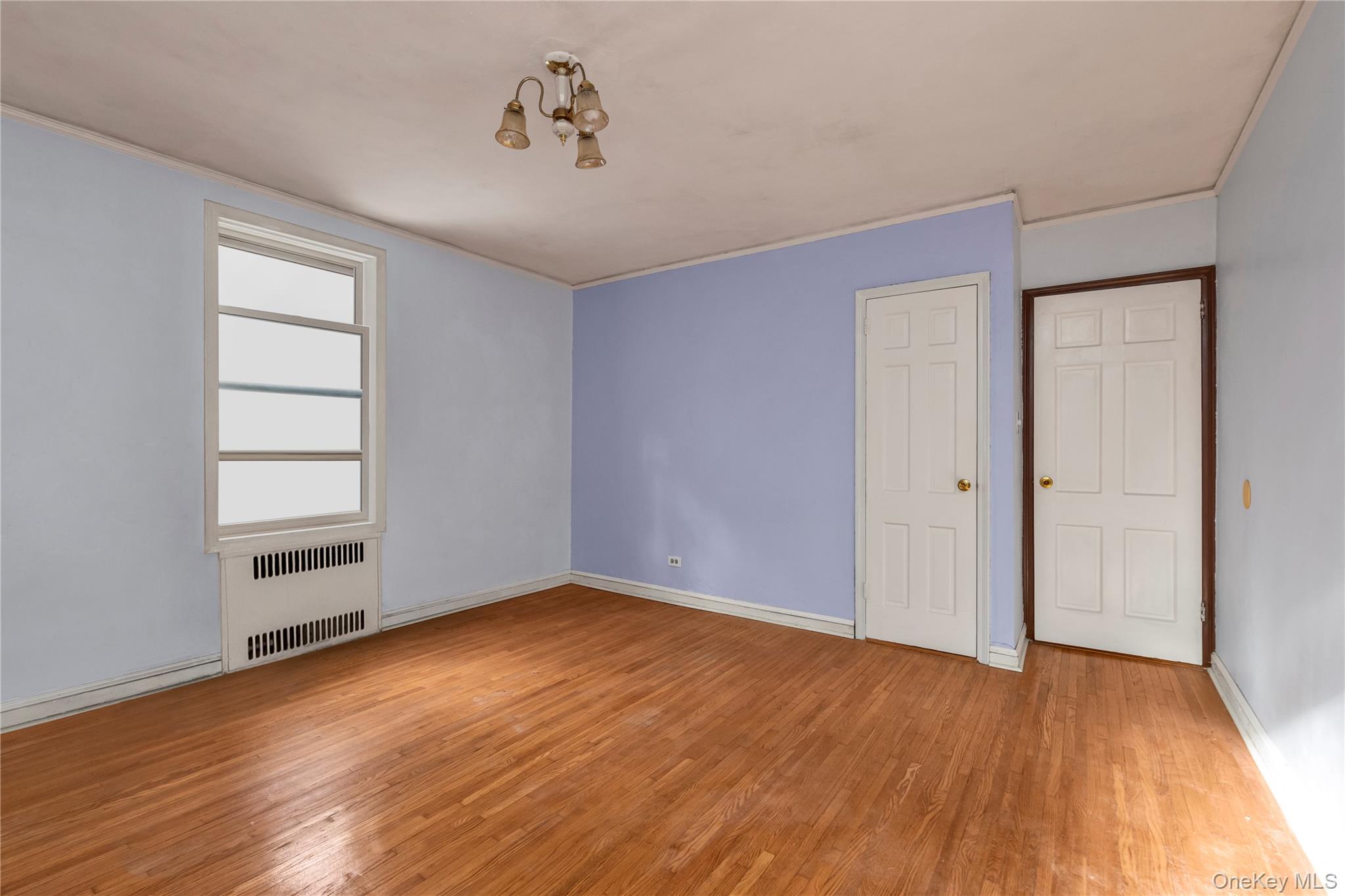 76-12 35th Avenue, Unit 1B Queens, NY 11372 - Photo 19 of 22 Spare room with light wood finished floors, radiator heating unit, and a chandelier