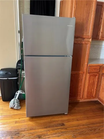 a view of a refrigerator in kitchen and an empty room with wooden floor