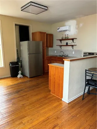 a view of a refrigerator in kitchen and an empty room with wooden floor