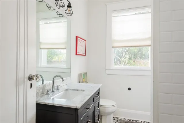 a bathroom with a granite countertop sink a toilet and a window