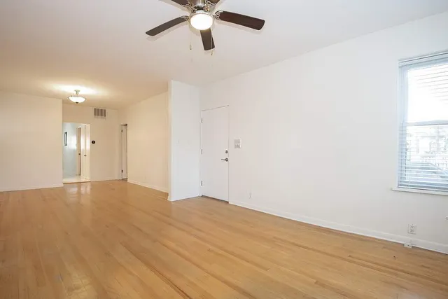an empty room with wooden floor fan and windows
