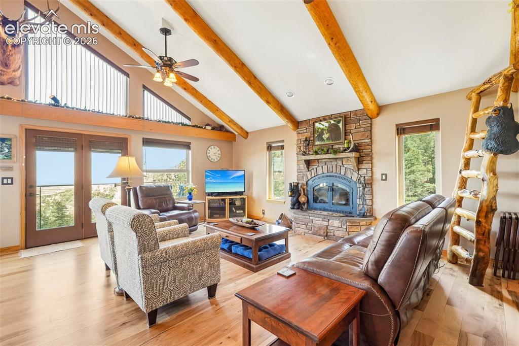 858 Oak Ridge Road Manitou Springs, CO 80829 - Photo 12 of 50 Open concept living room with tall vaulted-wood beamed ceilings, a wood burning fireplace, with a wall of windows giving you views of the mountains and city while bringing a nice touch of natural light inside , a walk out to the concrete wrap around deck all surrounded by solid hickory flooring