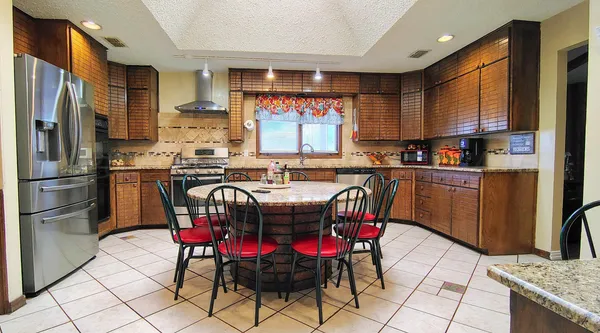a kitchen with stainless steel appliances granite countertop a dining table chairs refrigerator and sink