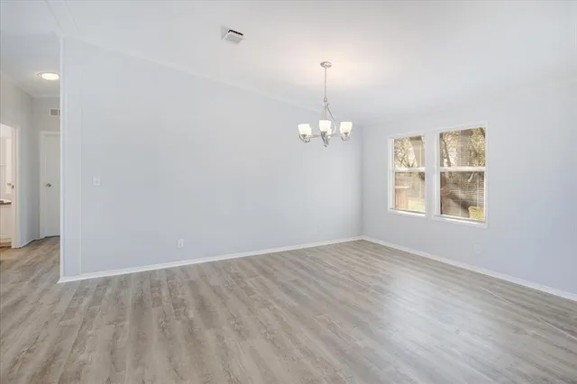 an empty room with wooden floor chandelier and windows