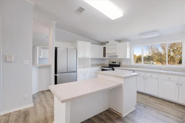 a kitchen with stainless steel appliances a sink a stove a refrigerator cabinets and a window