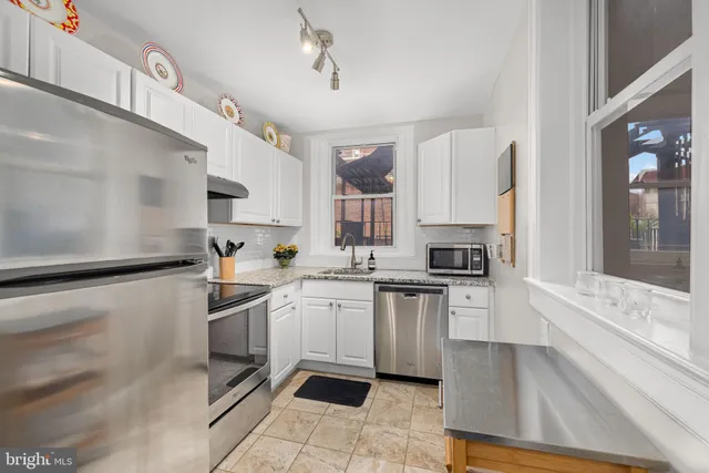 a kitchen with stainless steel appliances a sink a stove a refrigerator cabinets and a window