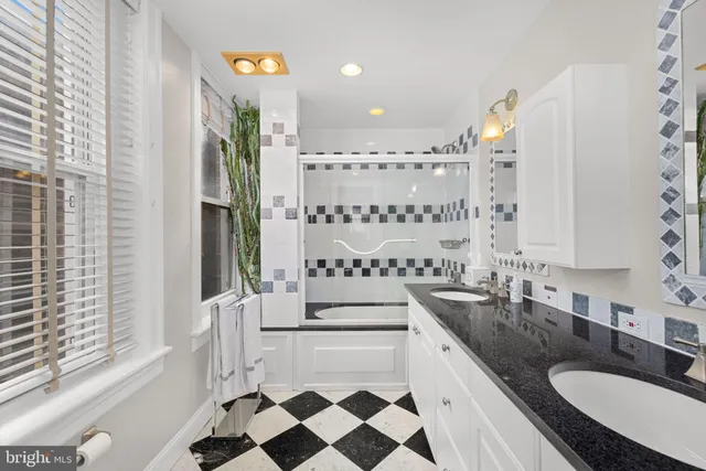 a bathroom with a granite countertop double vanity sink a mirror a bathtub and next to a window