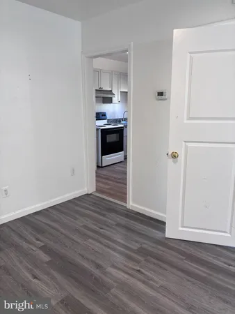 an empty room with wooden floor kitchen view and a window