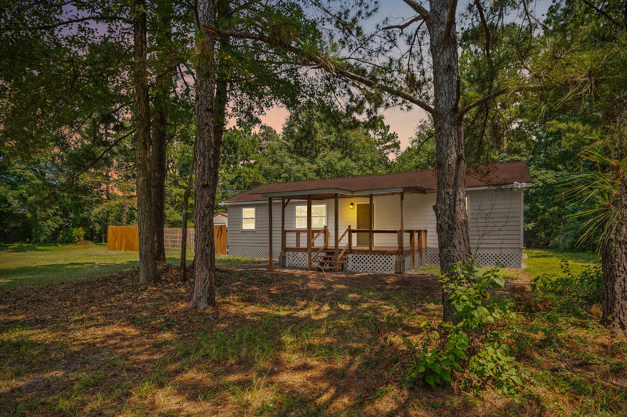 61 Hicks Loop West Cleveland, TX 77328 - Photo 2 of 38 Charming cottage nestled among mature trees, featuring a cozy front porch and a serene, wooded backdrop.