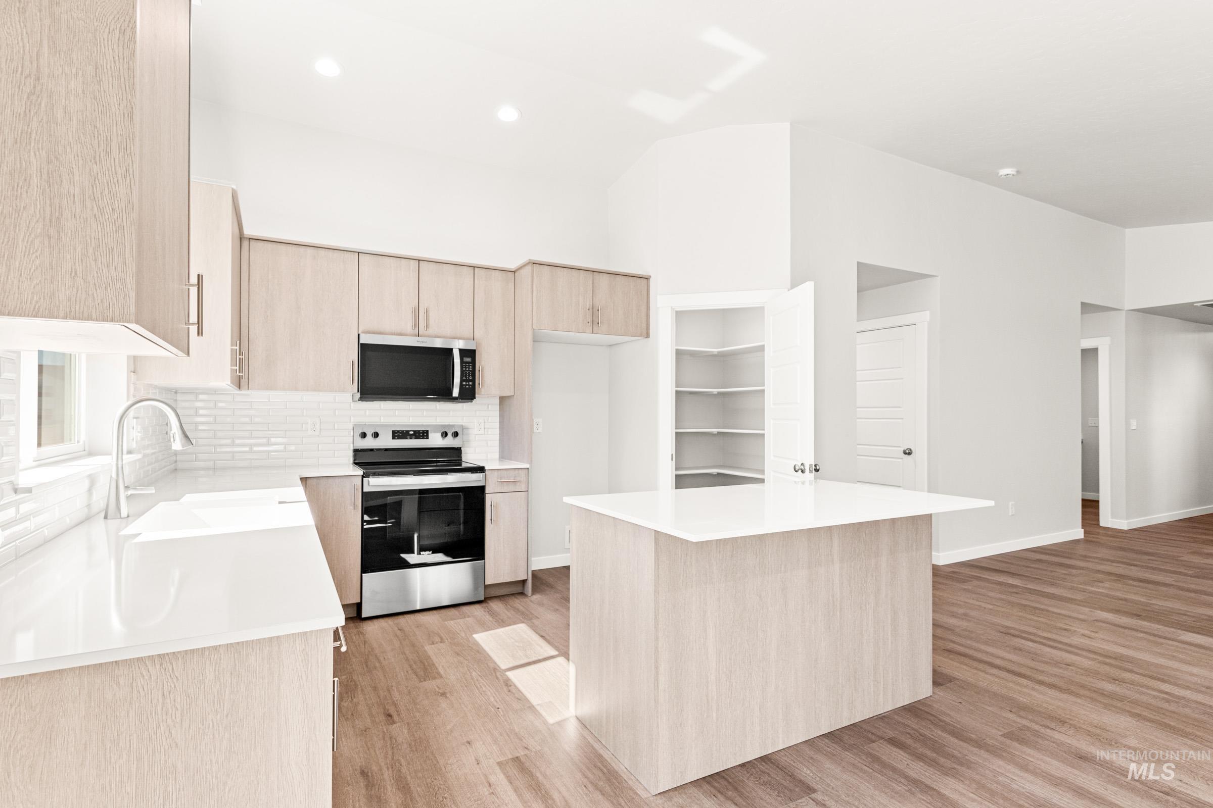 1077 West Jasper Street Meridian, ID 83642 - Photo 6 of 19 Kitchen featuring a central island with white countertop, stainless steel appliances, light wood-finish cabinetry, white subway tile backsplash, and wood-finish flooring