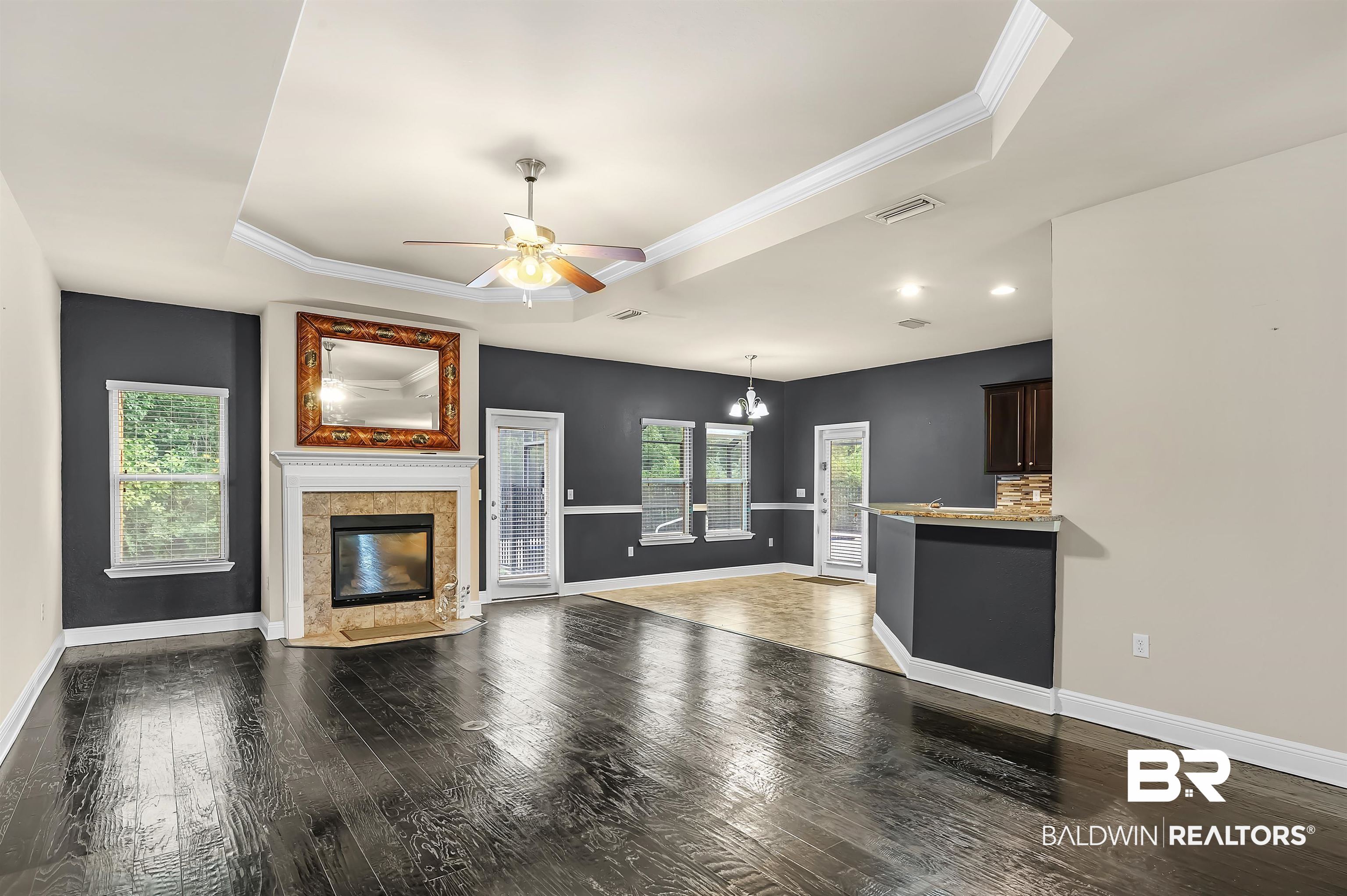 1086 Melbourne Court Foley, AL 36535 - Photo 7 of 43 Unfurnished living room with crown molding, a tiled fireplace, ceiling fan with notable chandelier, dark wood-type flooring, and a raised ceiling