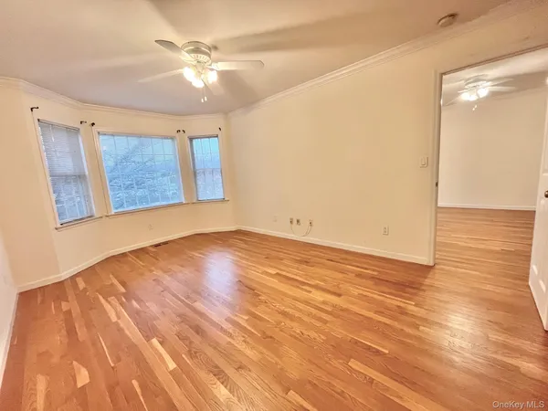 a view of an empty room with wooden floor and a ceiling fan