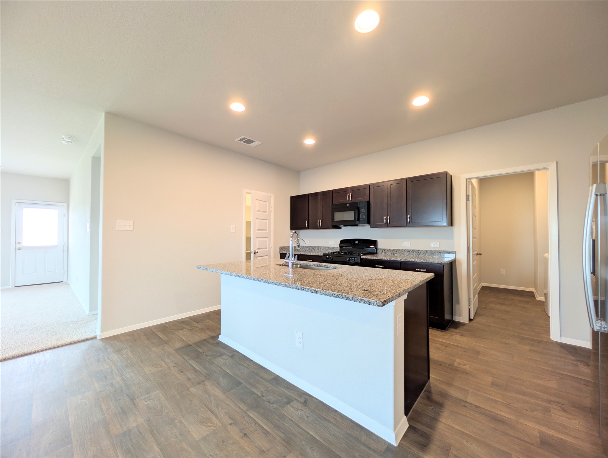 5524 Sacra Cove Austin, TX 78747 - Photo 8 of 37 Kitchen featuring dark wood finish cabinets, a kitchen island with sink, black appliances, light stone countertops, and dark wood-type flooring