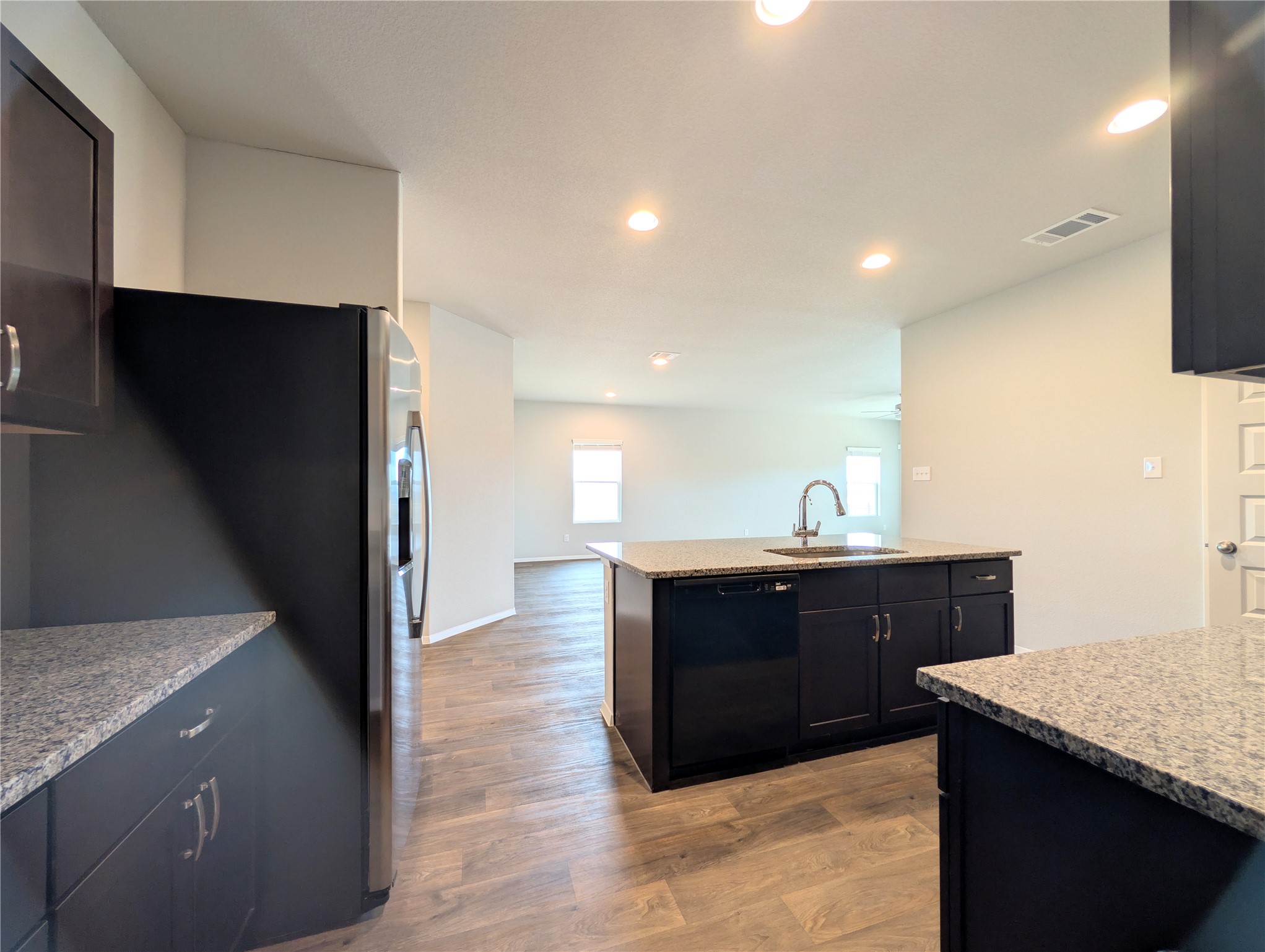 5524 Sacra Cove Austin, TX 78747 - Photo 9 of 37 Kitchen with light stone countertops, dark wood finished floors, black dishwasher, stainless steel refrigerator with ice dispenser, and recessed lighting