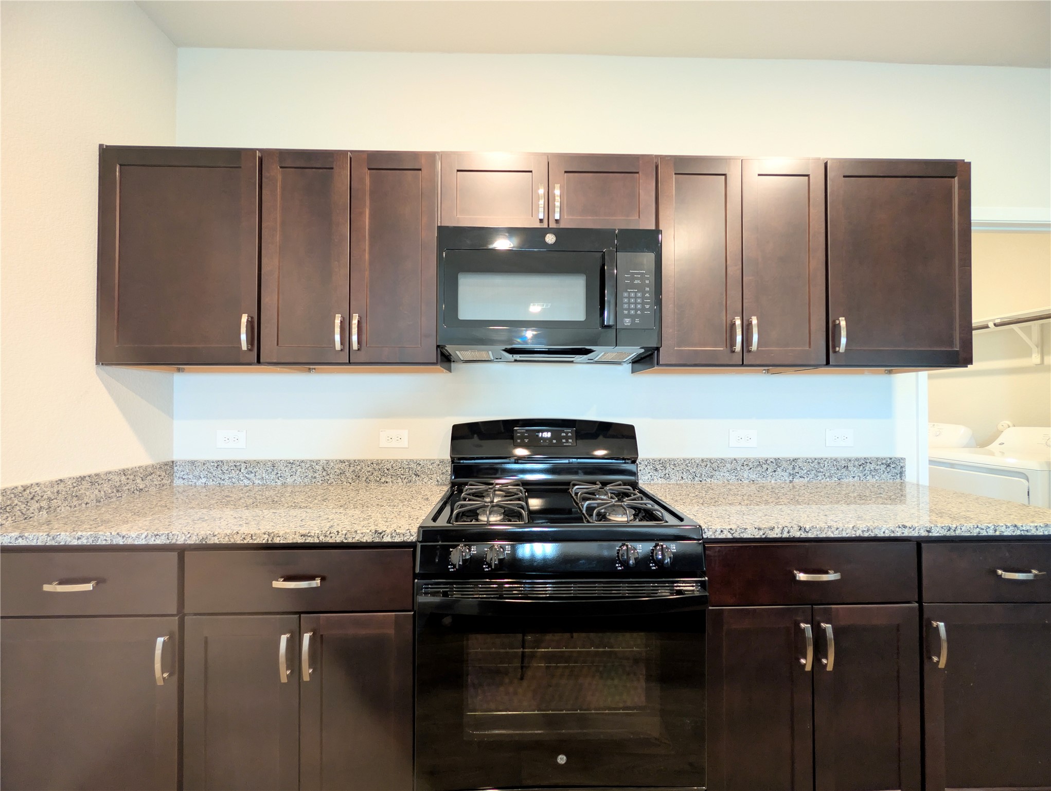 5524 Sacra Cove Austin, TX 78747 - Photo 10 of 37 Kitchen with black appliances, dark wood finish cabinetry, light stone counters, and washing machine and clothes dryer