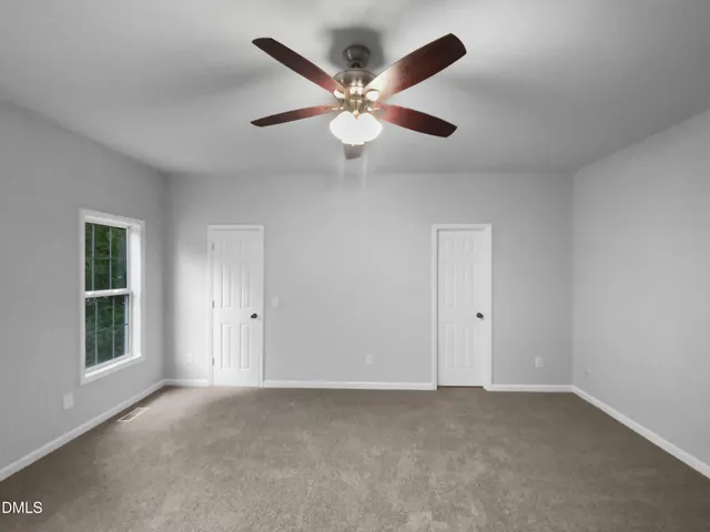 a view of an empty room with window and ceiling fan