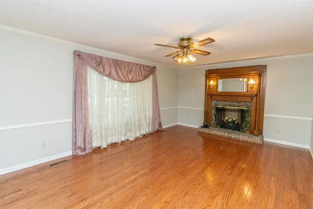 a view of a livingroom with a fireplace a ceiling fan and wooden floor
