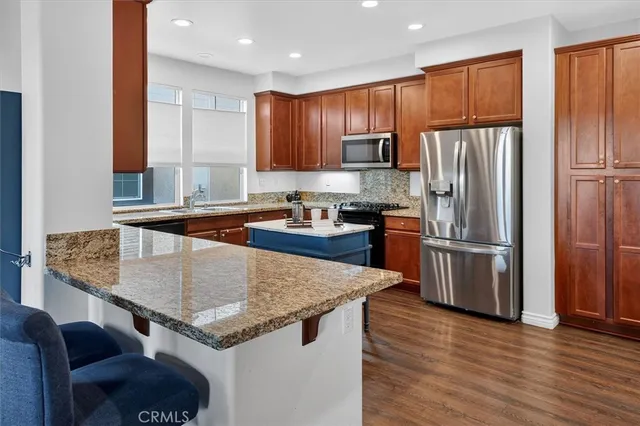 a kitchen with stainless steel appliances granite countertop a refrigerator a sink dishwasher a stove and a refrigerator with wooden floor