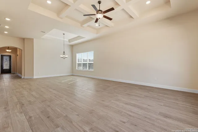 an empty room with wooden floor ceiling fan and windows