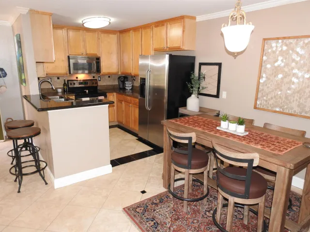 a kitchen with stainless steel appliances kitchen island granite countertop a dining table chairs and a refrigerator
