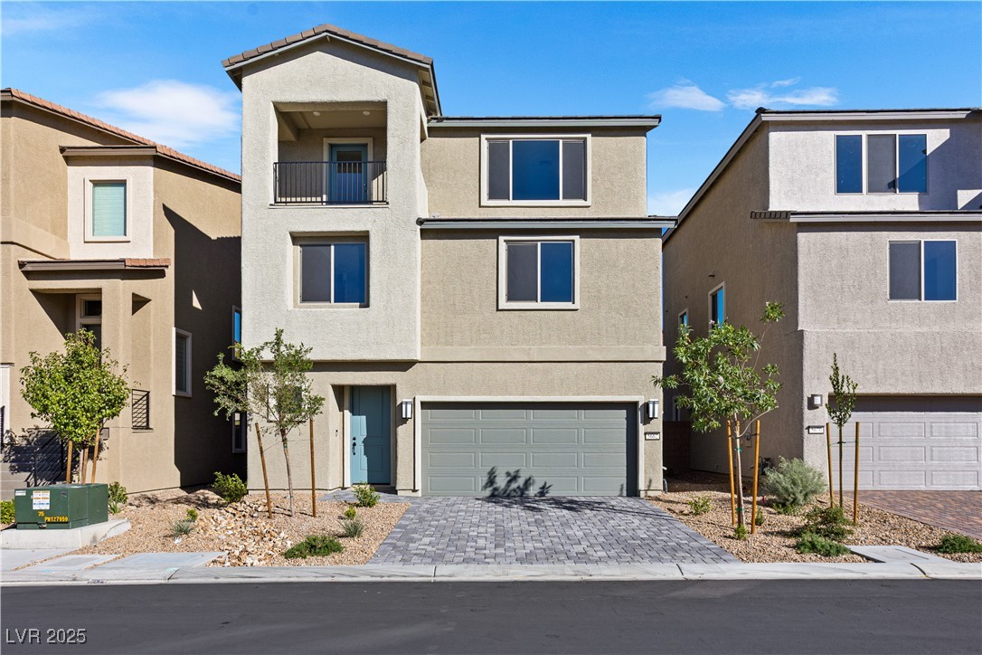 View of front of home with stucco siding, an attached garage, decorative driveway, and a balcony