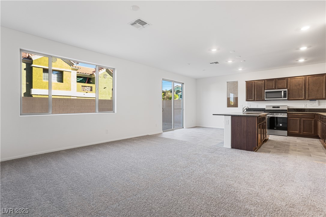 5662 Spring Trellis Street Las Vegas, NV 89113 - Photo 21 of 21 Kitchen with dark countertops, dark brown cabinets, open floor plan, a center island with sink, and light colored carpet